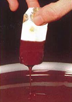 Fingers dipping a portion of nougat into chocolate.